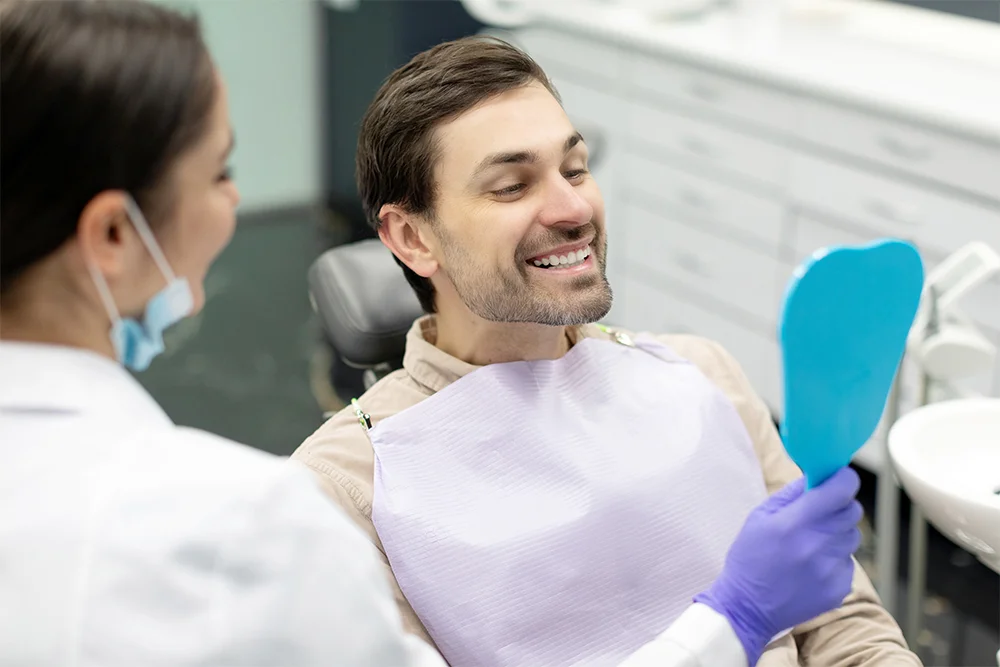 Happy-man-looking-at-mirror-after-teeth-treatment